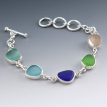 Gorgeous rare, aqua and cobalt blue sea glass gems star in this five piece, genuine sea glass bracelet bezel set in sterling silver. The colors are beautifully complementary starting (from l to r) with a luscious lavender, fun lime green, dark cobalt blue, fantastic deep aqua and sweet peachy/pink. Our genuine sea glass bracelet is a gift that your sea glass lover will cherish forever. It is adjustable from 7-8" with its versatile toggle clasp. Pure sea glass for pure joy, it is genuine, beach found and guaranteed to please. We offer a money back guarantee if you are not completely satisfied. Plus fast, free shipping, free gift wrap, and an anti-tarnish storage bag. • Metal: Sterling Silver • Origin of Sea Glass: Puerto Rico & Hawaii • Rarity: Deep Aqua and Cobalt Are Rare to Extremely Rare; Pink, Lavender and Lime are Rare • Size of Sea Glass: Sizes range 3/8" to 1/2" • Bracelet Length: Adjustable from 7-8" [cc_product sku="bz11" display="inline" quantity="true" price="true"] View All Sea Glass Bezel Set Bracelets. Genuine Sea Glass. Sterling Silver. Ready for Fast, Free Shipping.